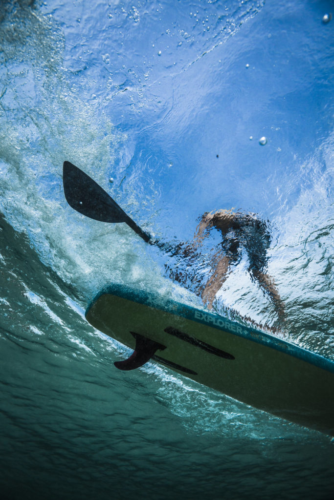 a shot of a person on a paddleboard taken from underwater.